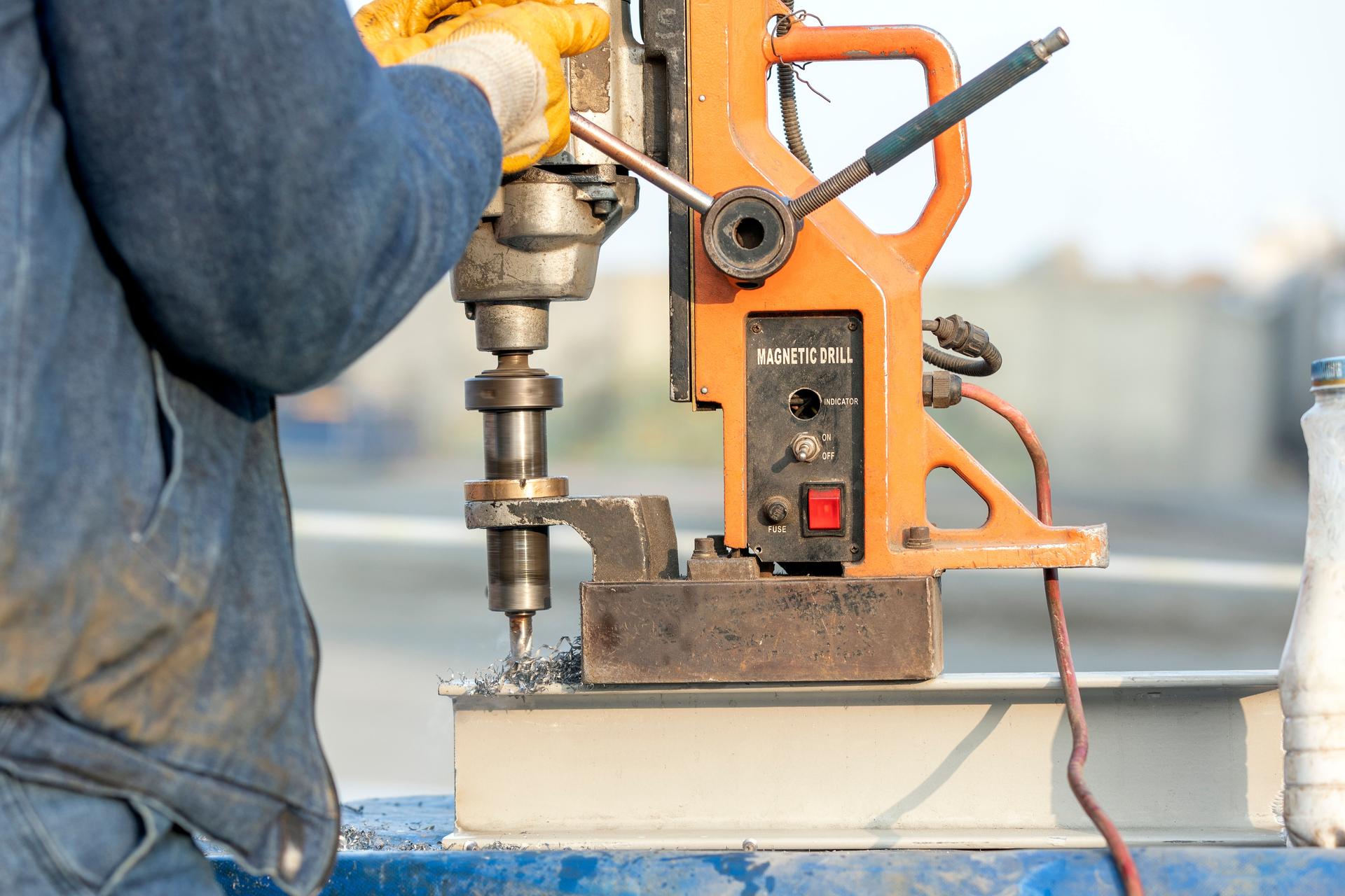The worker is using a magnetic drilling machine for drill to steel material. It is a portable drilling machine with a magnetic base (either electromagnetic or permanent magnet).