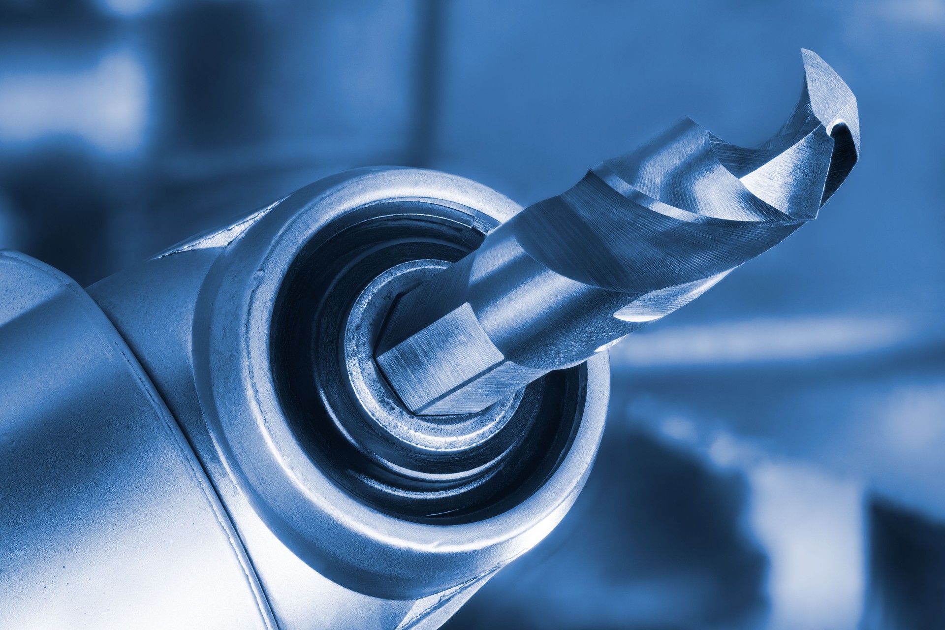 Sharp tip of drill bit clamped in cordless machine chuck with right angle head in blue tone on blurred tech background