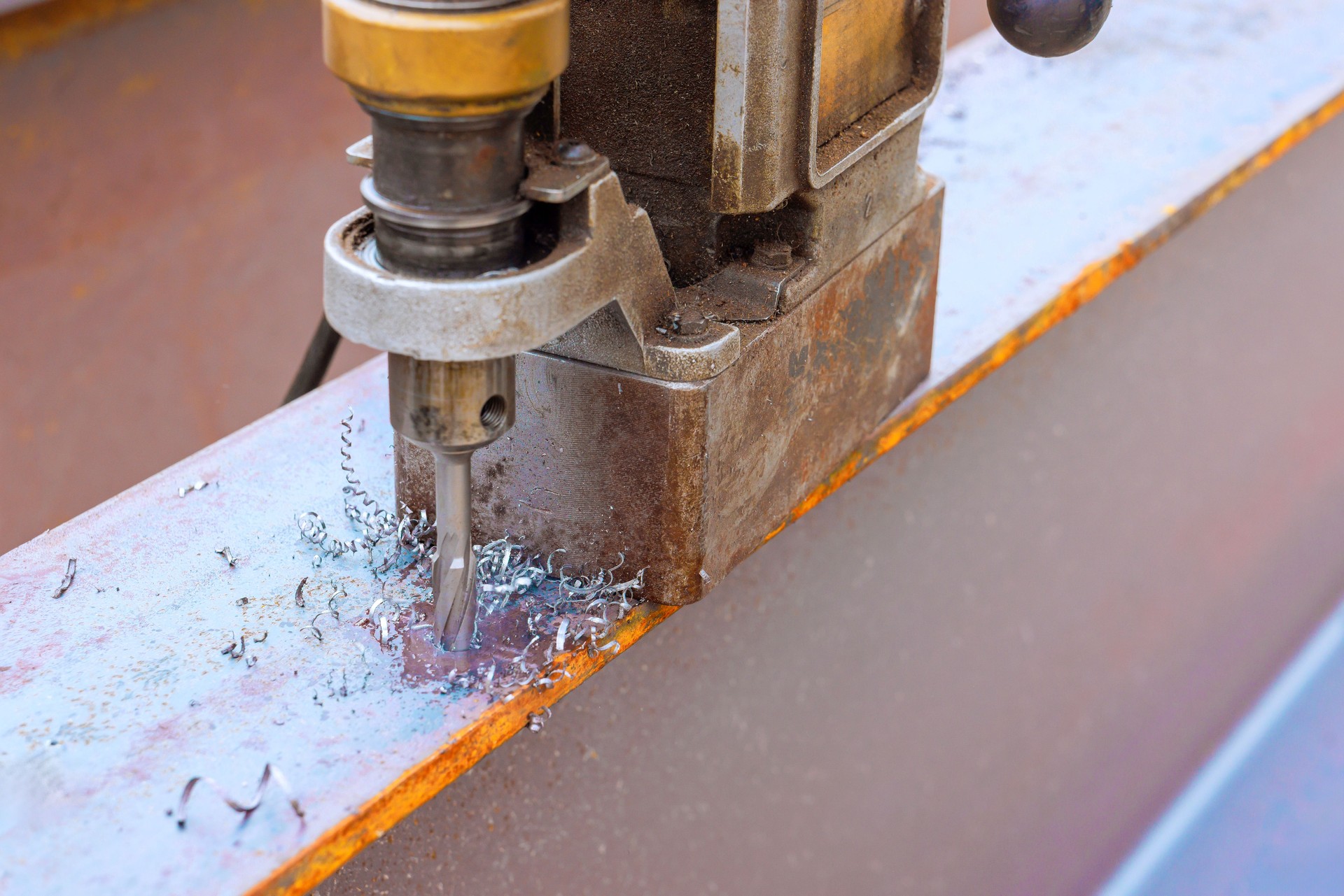 Metalworking process in workshop highlighting drilling into steel plate with metal shavings machinery