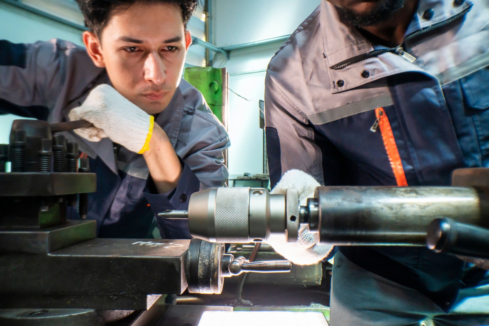 Two focused industrial technicians work together operating heavy machinery in a workshop. The image of teamwork, precision, and technical expertise in an engineering and manufacturing industry